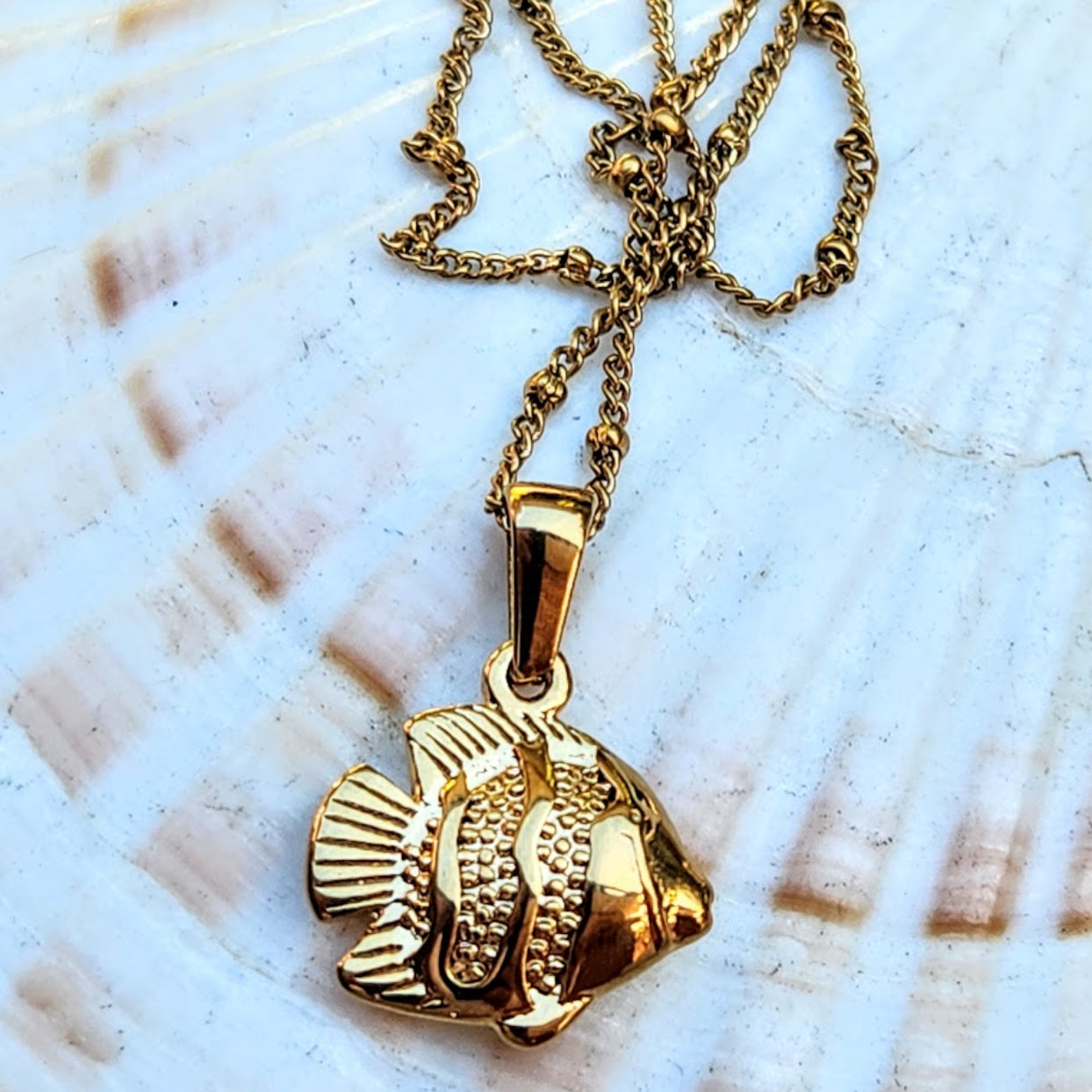 Gold fish pendant necklace on a shell background