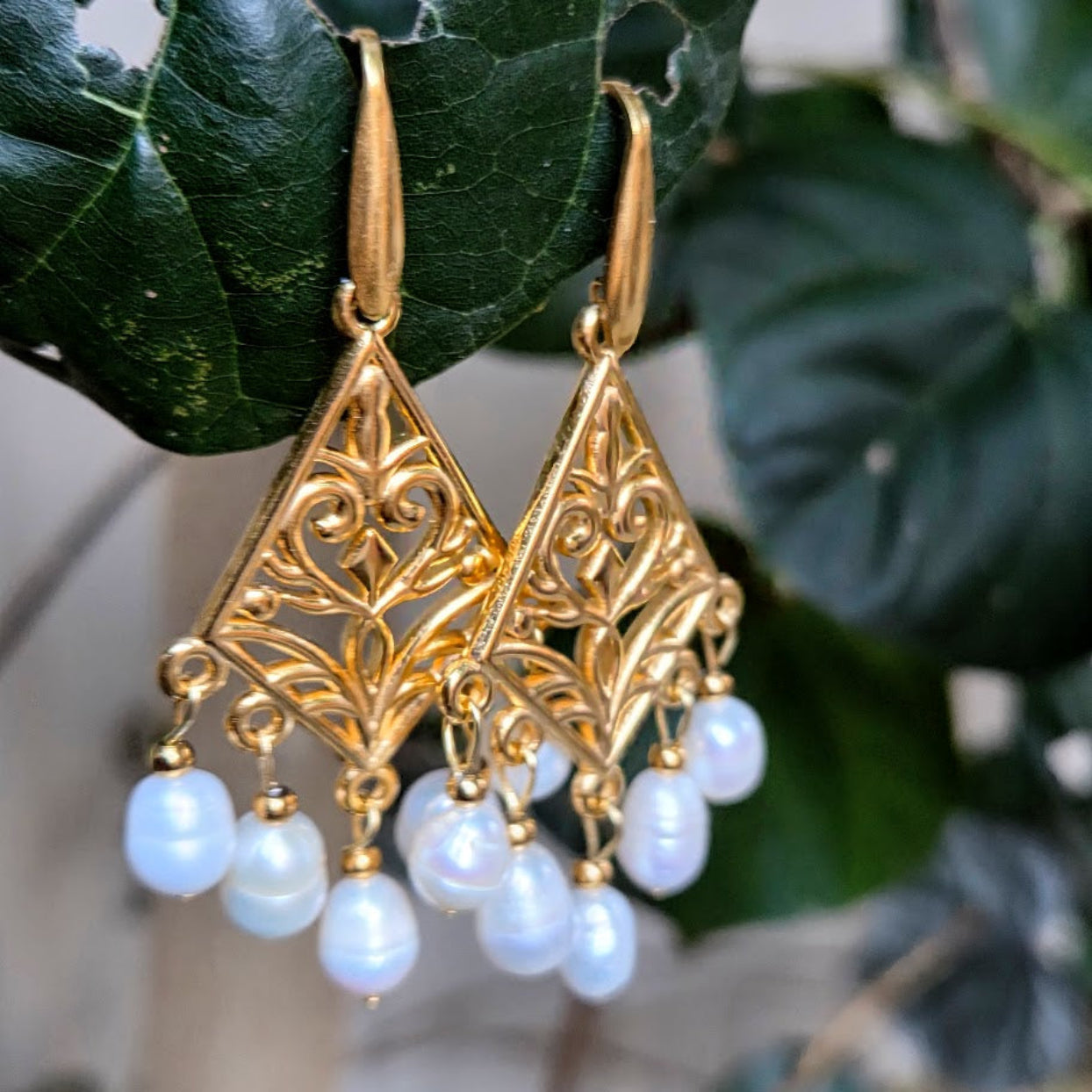Gold earrings with pearl drops on a leaf background