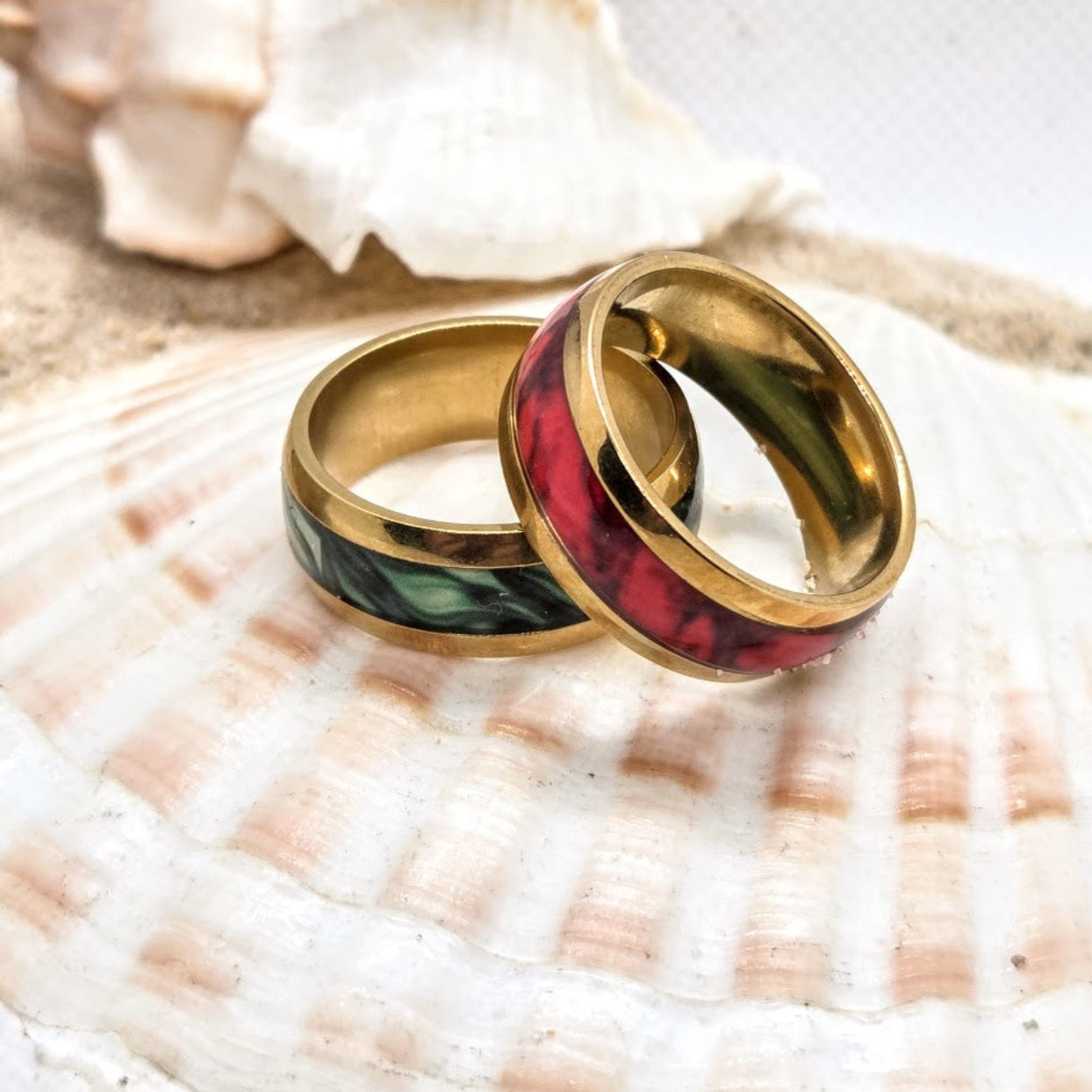 Two gold-rimmed rings with green and red inlay on a seashell.