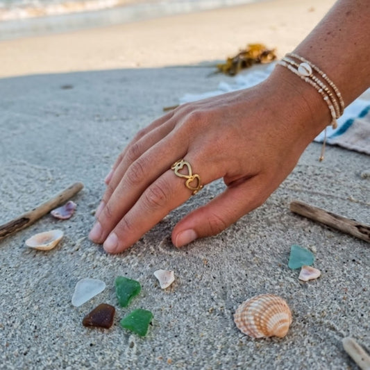 Hand with a gold ring on a sandy surface with seashells and driftwood.