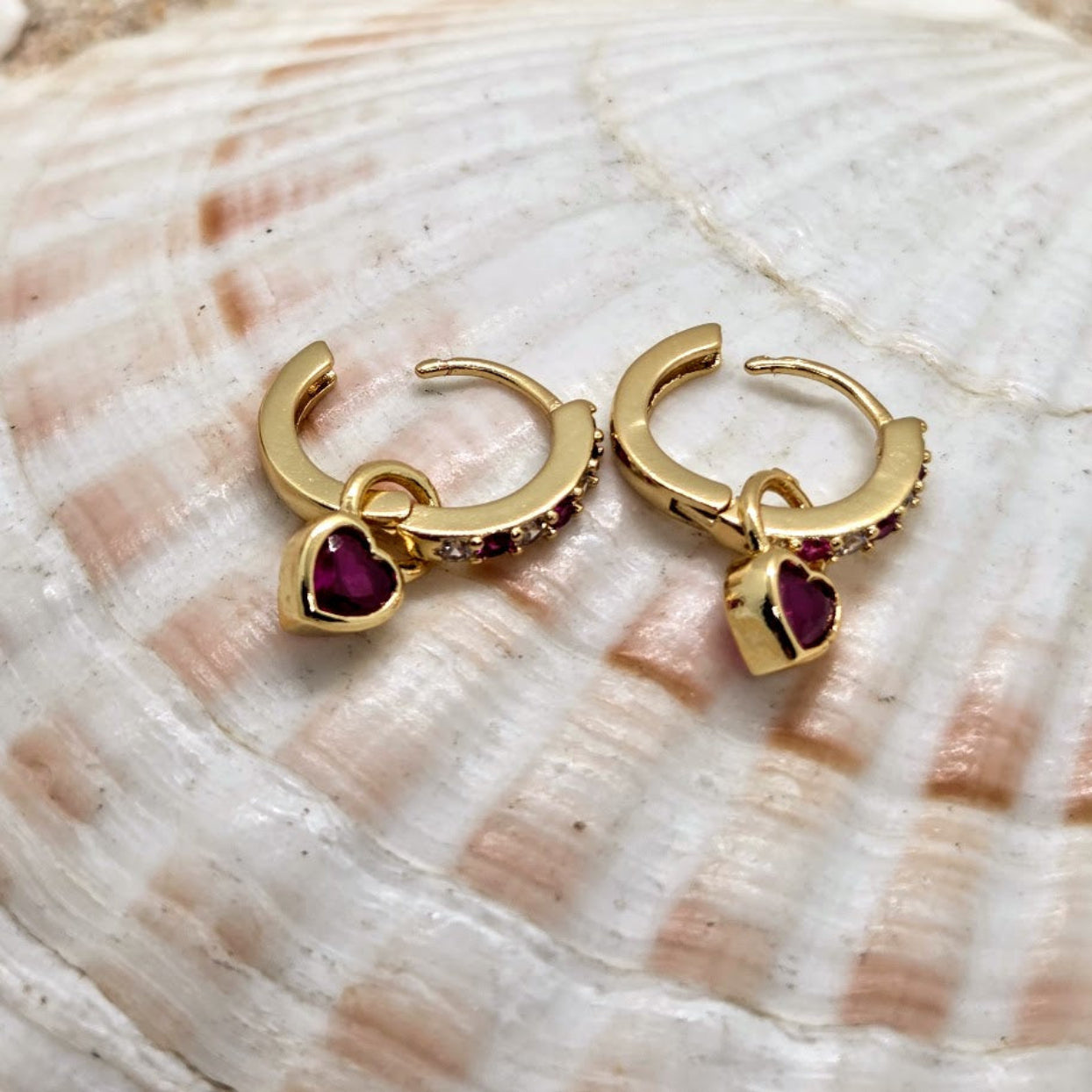 Gold hoop earrings with red gemstones on a shell background