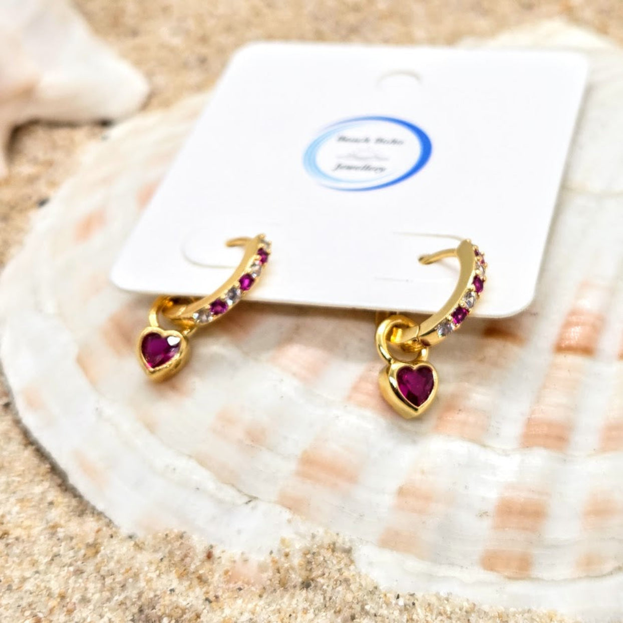 Gold hoop earrings with heart-shaped gemstones on a shell