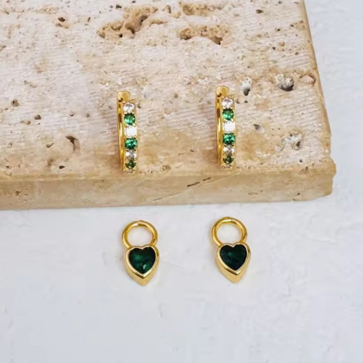 Gold hoop earrings with green gemstones on a stone surface