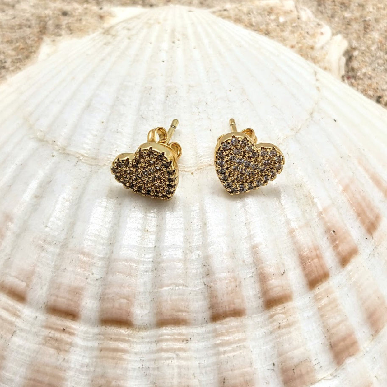Gold heart-shaped earrings on a shell