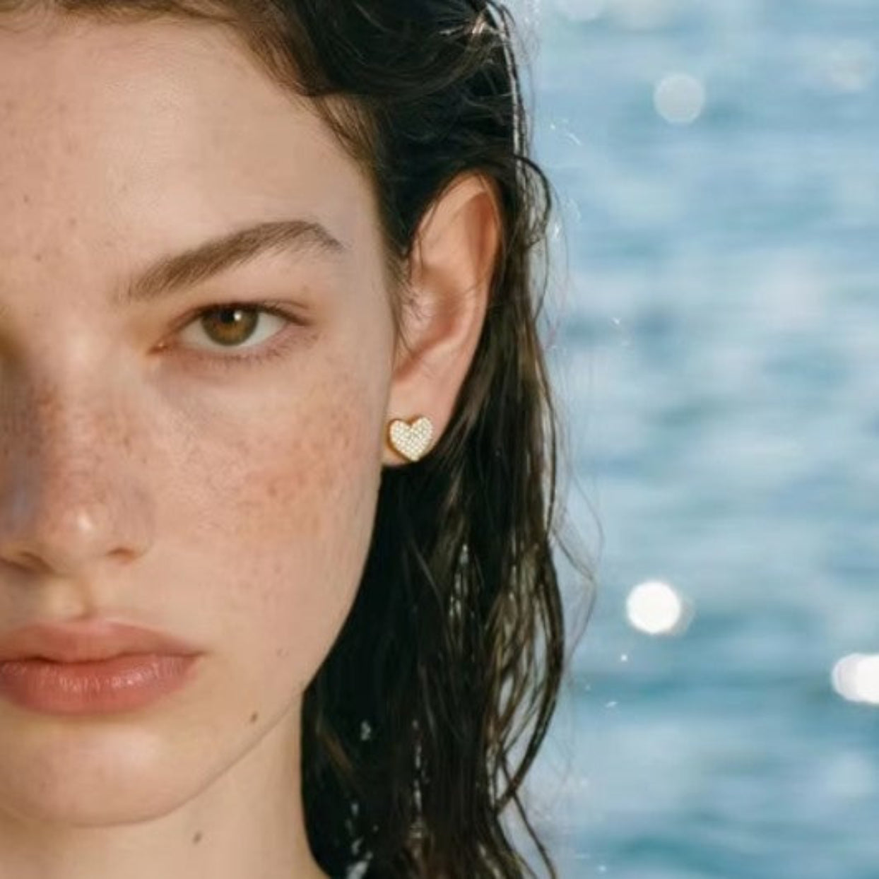 Close-up of a person wearing heart-shaped earrings with a blurred water background