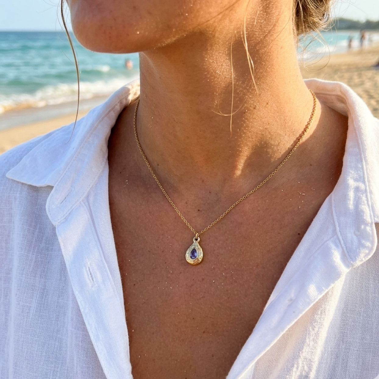Person wearing a gold necklace with a pendant on a beach