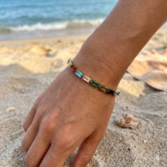 Hand wearing a colorful beaded bracelet on a sandy beach with ocean in the background