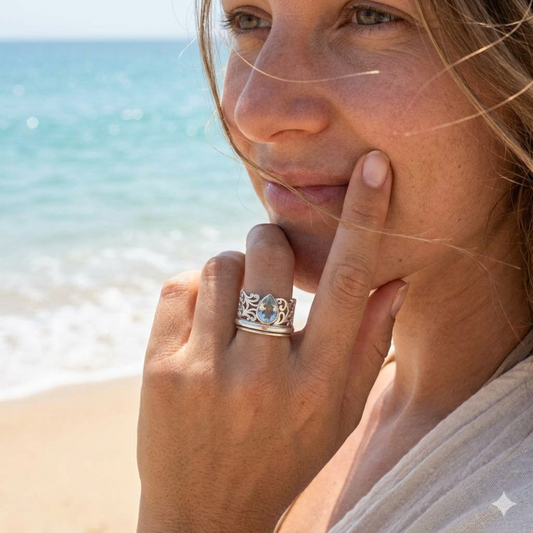 Woman on a beach wearing a silver ring with a blue gemstone.