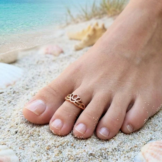 Foot wearing a toe ring on a sandy beach with shells and water in the background