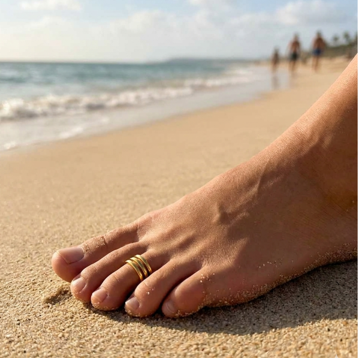 Foot with a gold ring on a sandy beach with ocean and people in the background