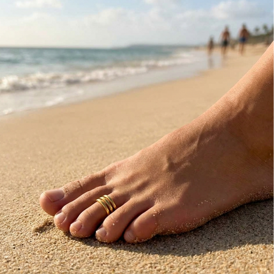 Foot with a gold ring on a sandy beach with ocean and people in the background