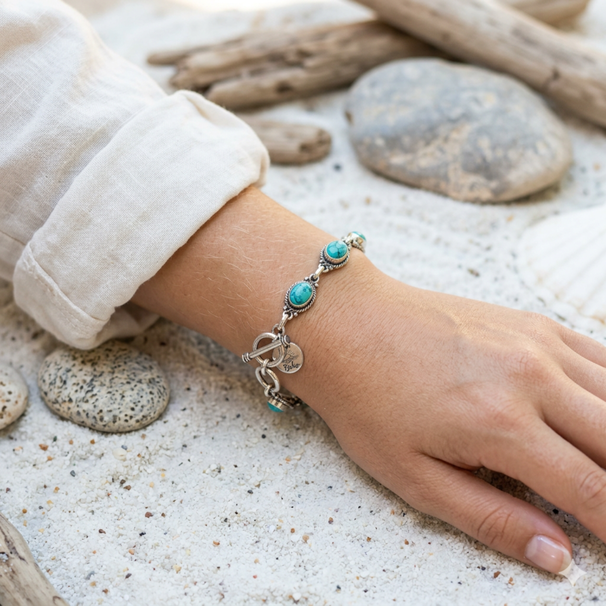 Hand wearing a silver bracelet with turquoise stones on a sandy background