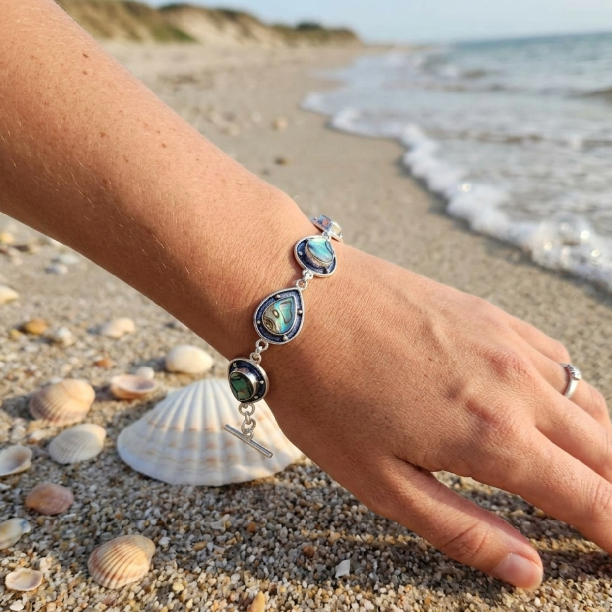 Hand wearing a bracelet on a beach with shells and ocean waves in the background