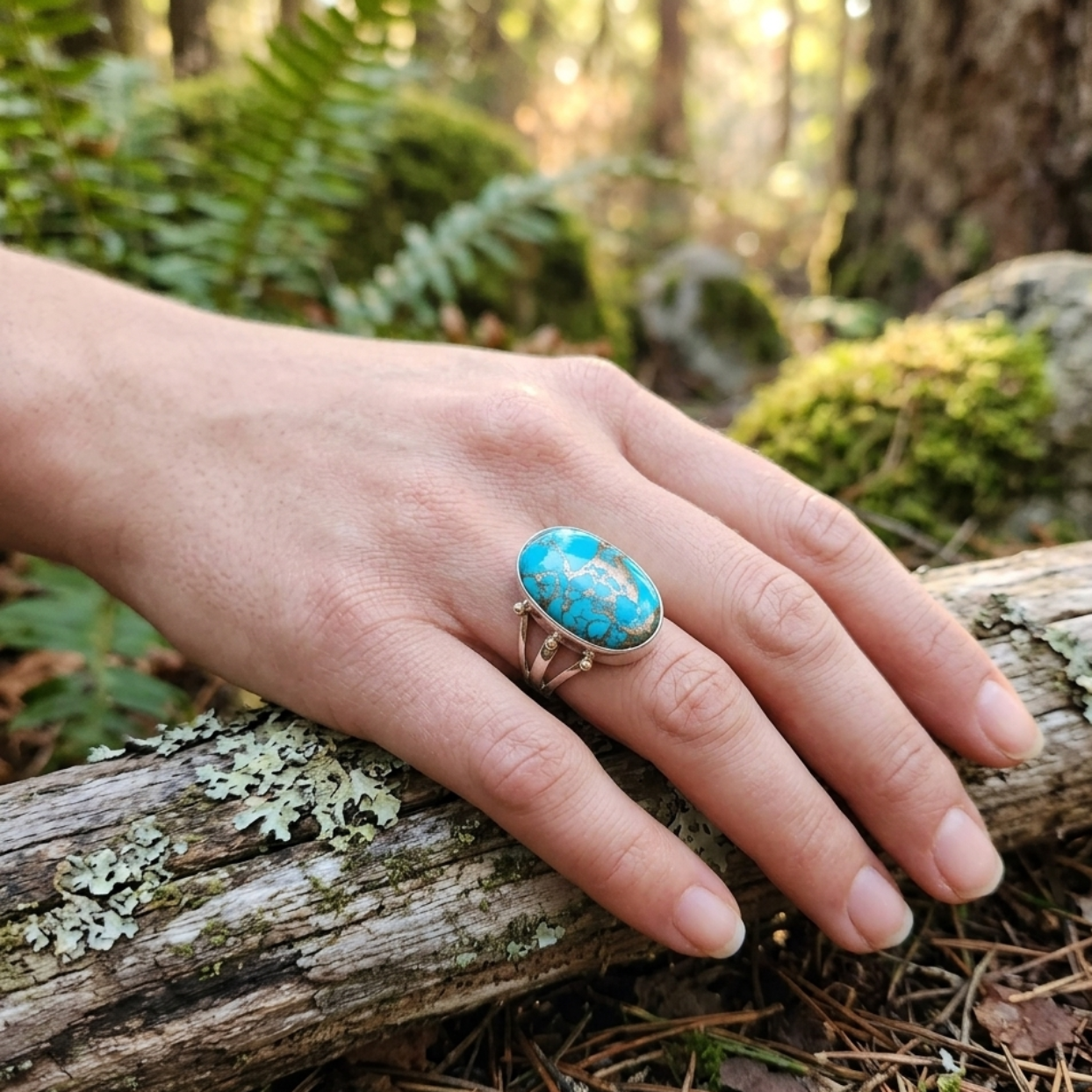 Hand wearing a turquoise ring on a log in a forest setting