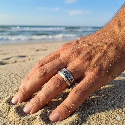 Hand with a ring on a sandy beach with ocean waves in the background