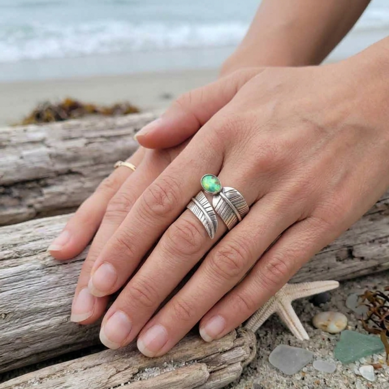 Hand wearing a silver ring with a green stone on a beach