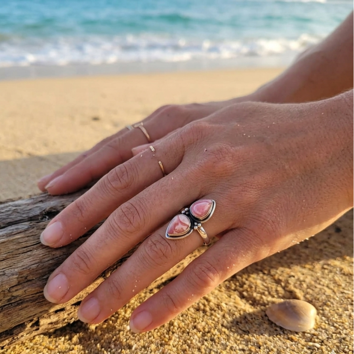 Hand wearing a ring with pink stones on a beach