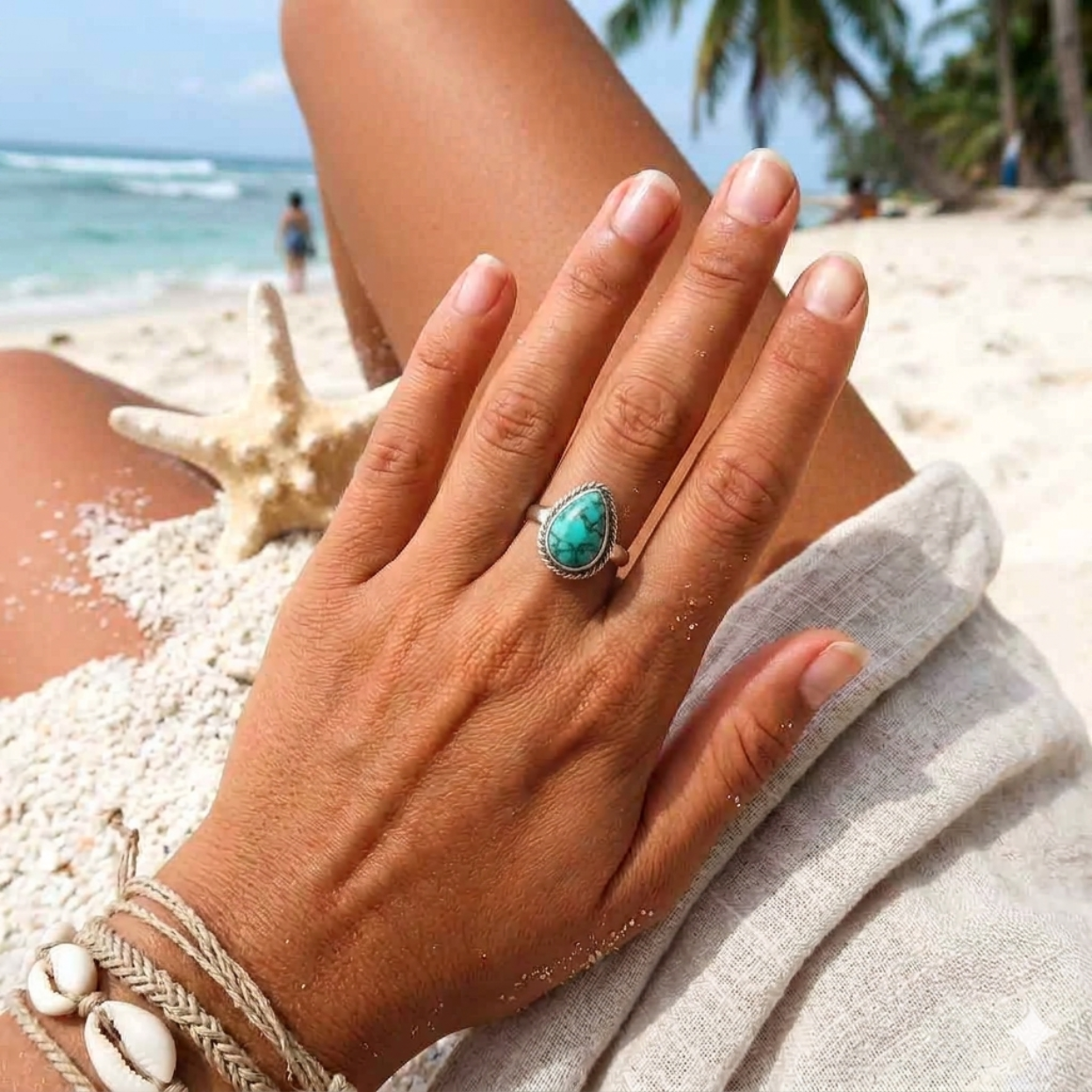 Hand wearing a turquoise ring on a beach with palm trees and ocean in the background