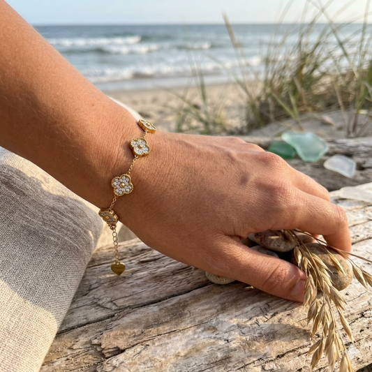 Hand wearing a gold bracelet on a beach with ocean and sand in the background