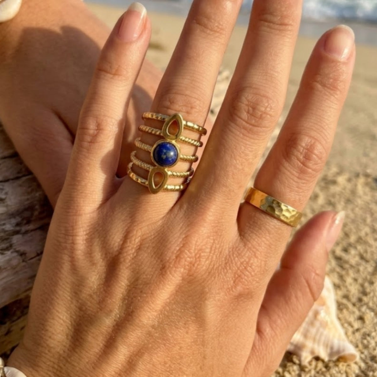 Hand wearing gold rings with a blue stone on a beach background