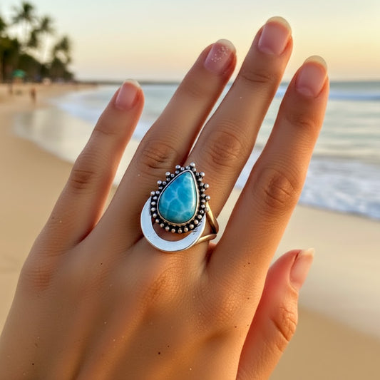 Hand wearing a turquoise ring with a beach in the background