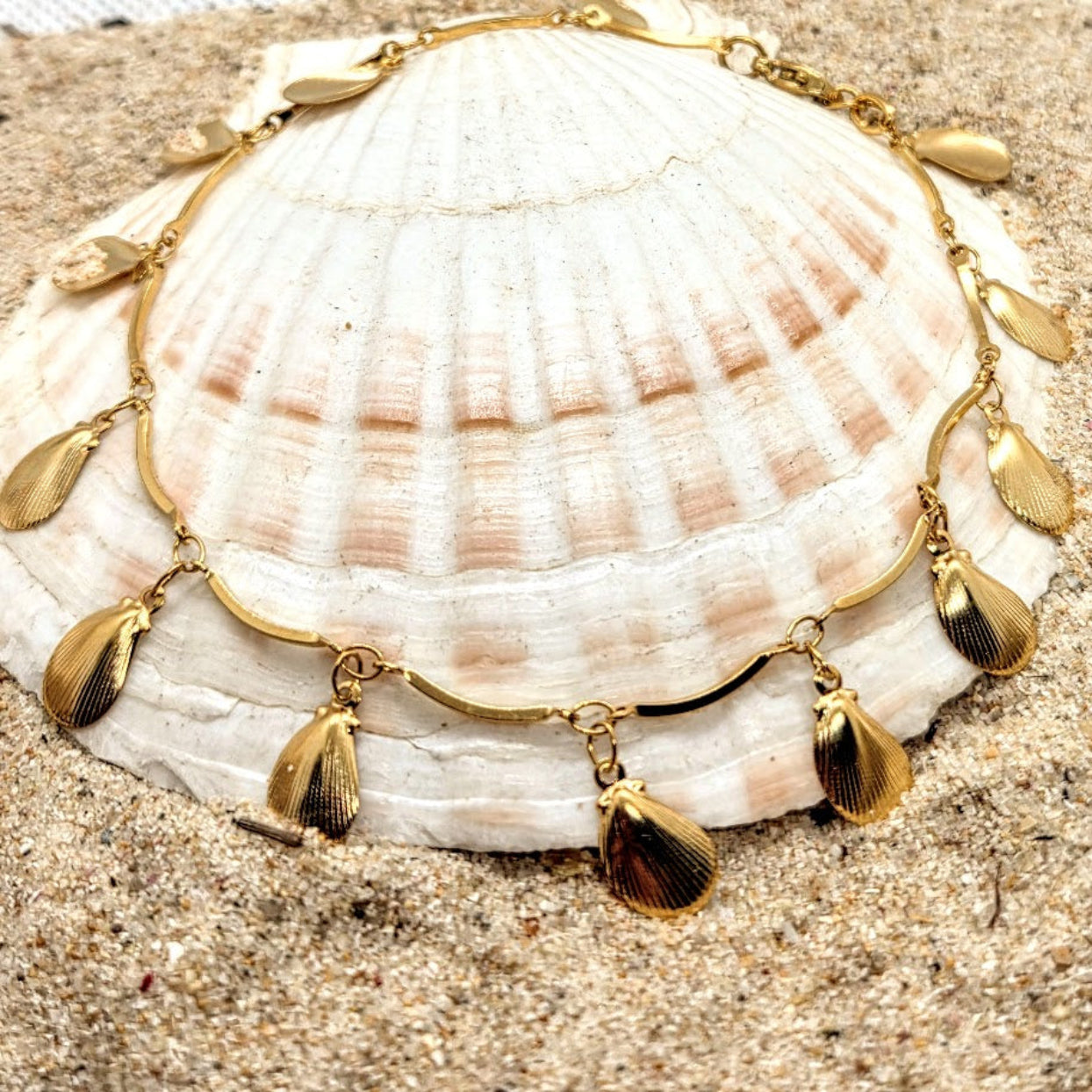 Gold necklace with pendant on a seashell on sand
