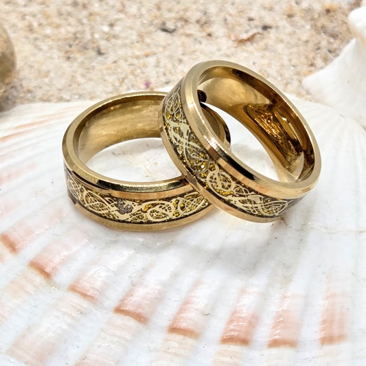 Two gold rings with intricate designs on a seashell background