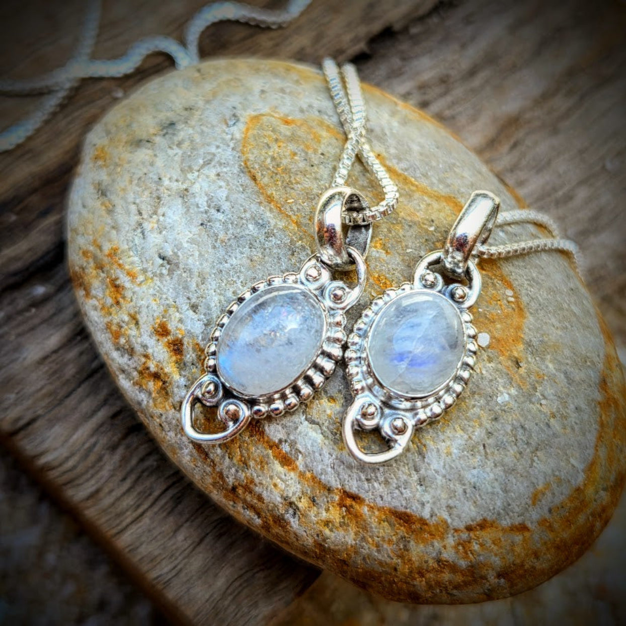 Two silver pendants with gemstones on a stone surface