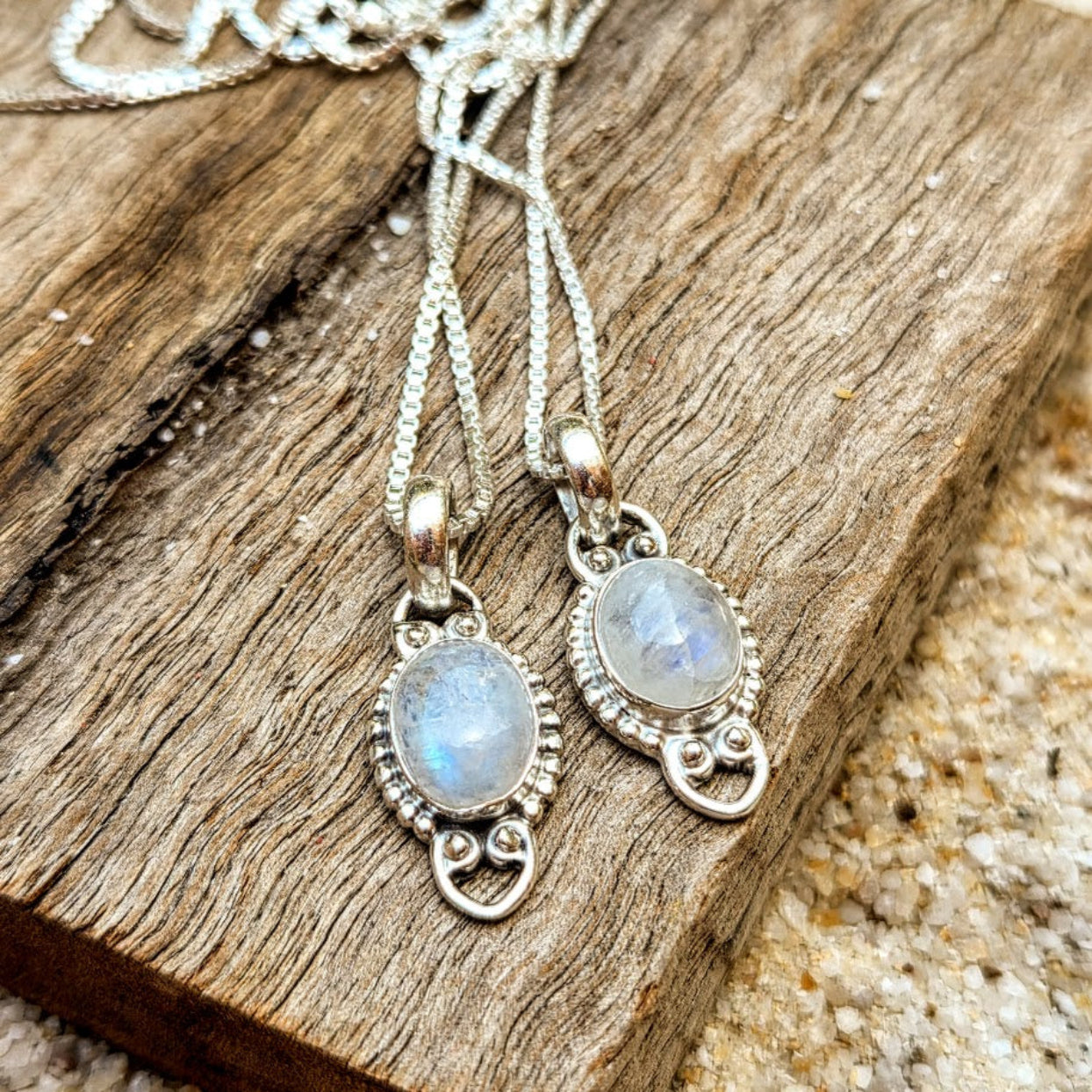 Two silver pendants with gemstones on a wooden surface