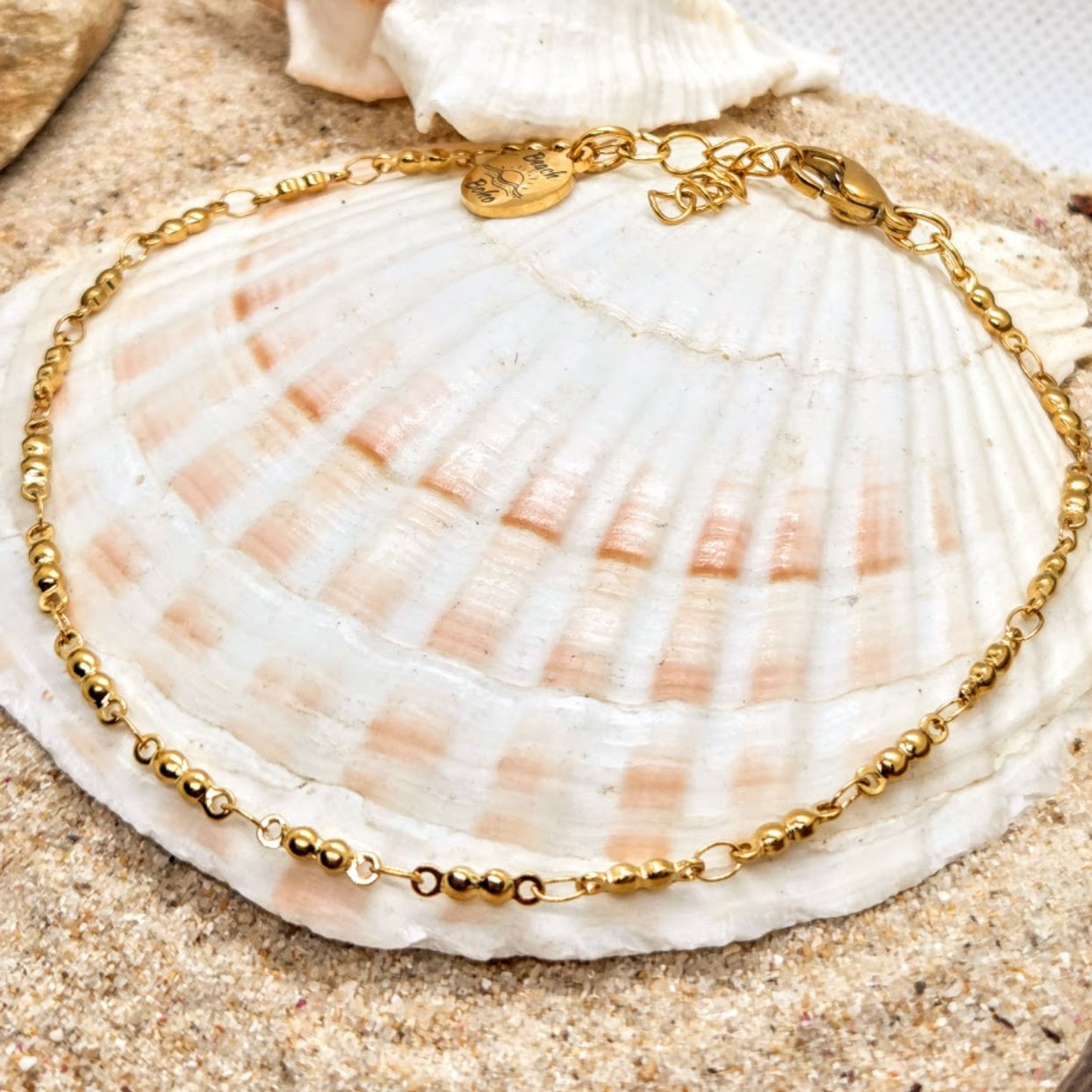 Gold bracelet on a seashell with sand background