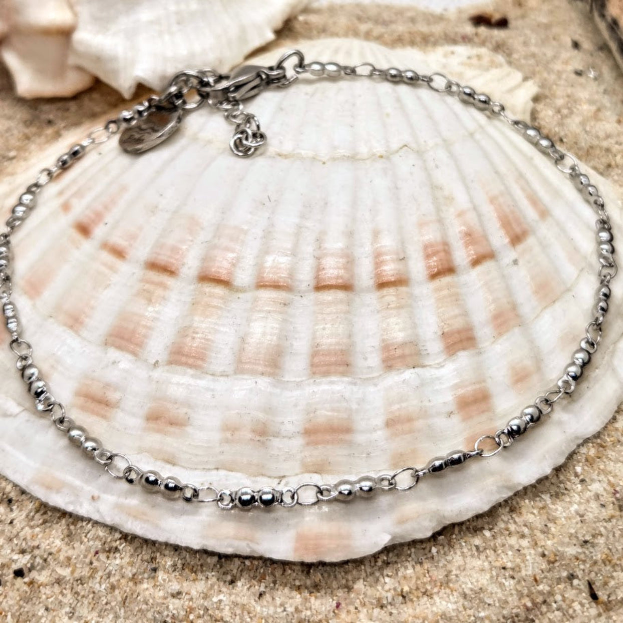 Silver bracelet on a seashell with sand in the background