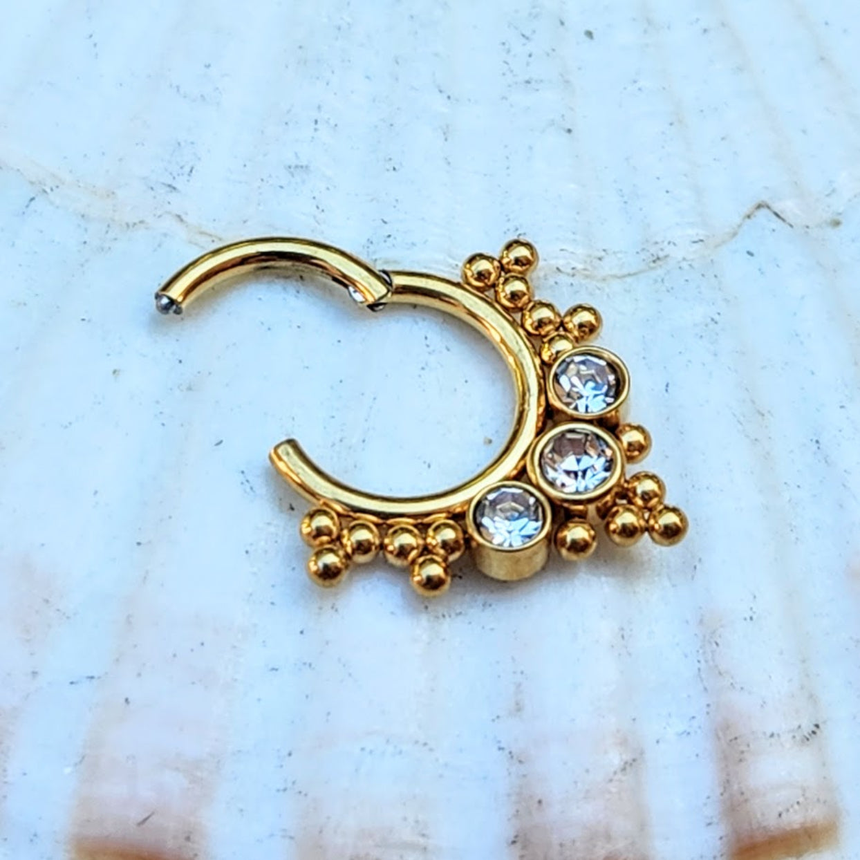 Gold nose ring with crystal stones on a light blue background