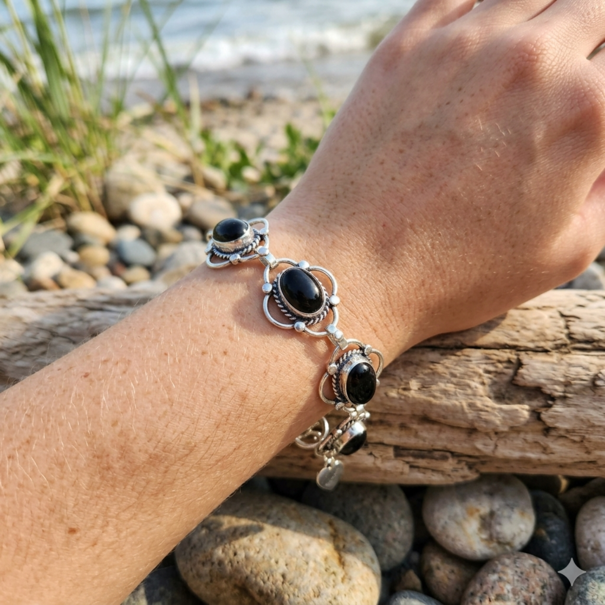 Hand wearing a silver bracelet with black stones on a beach.