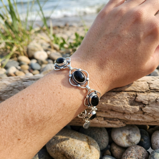 Hand wearing a silver bracelet with black stones on a beach.