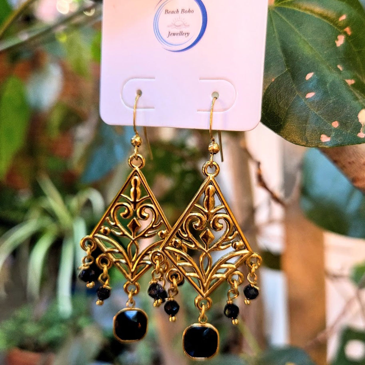 Gold and black earrings on a display card with a blurred green leafy background