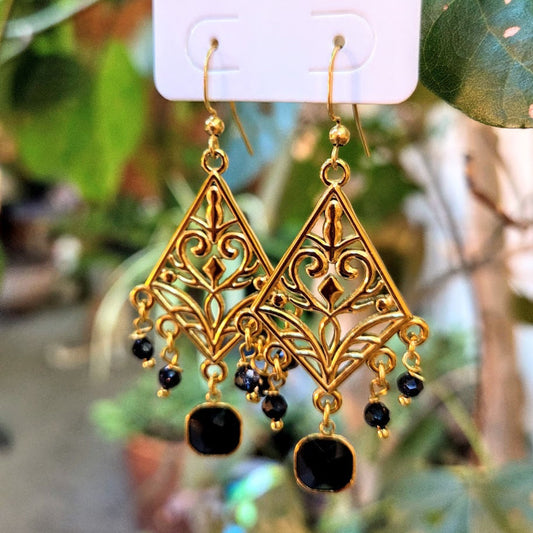 Gold earrings with black beads on a white card against a blurred natural background