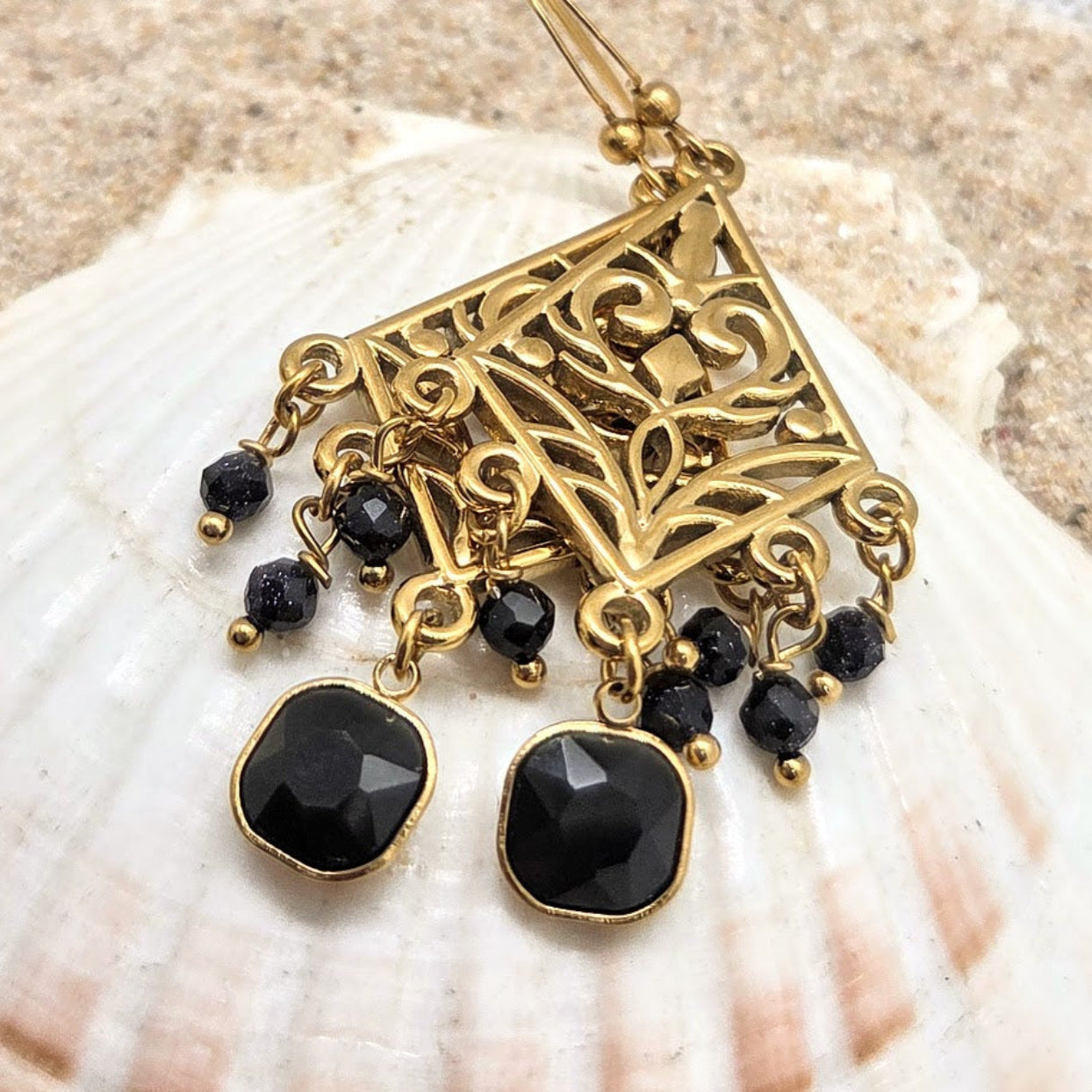 Gold earrings with black beads on a shell background