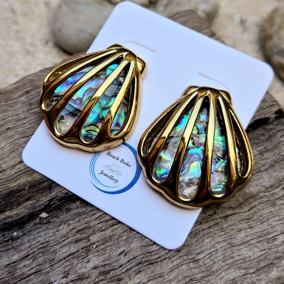 Gold shell-shaped earrings with abalone interior on a branded card, placed on wooden surface.