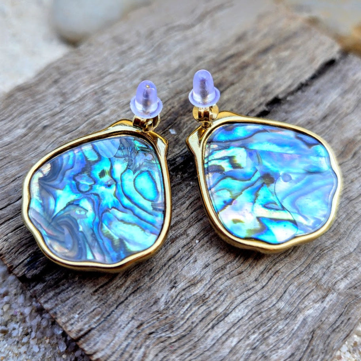 Pair of earrings with blue marbled design and gold frame on wooden surface