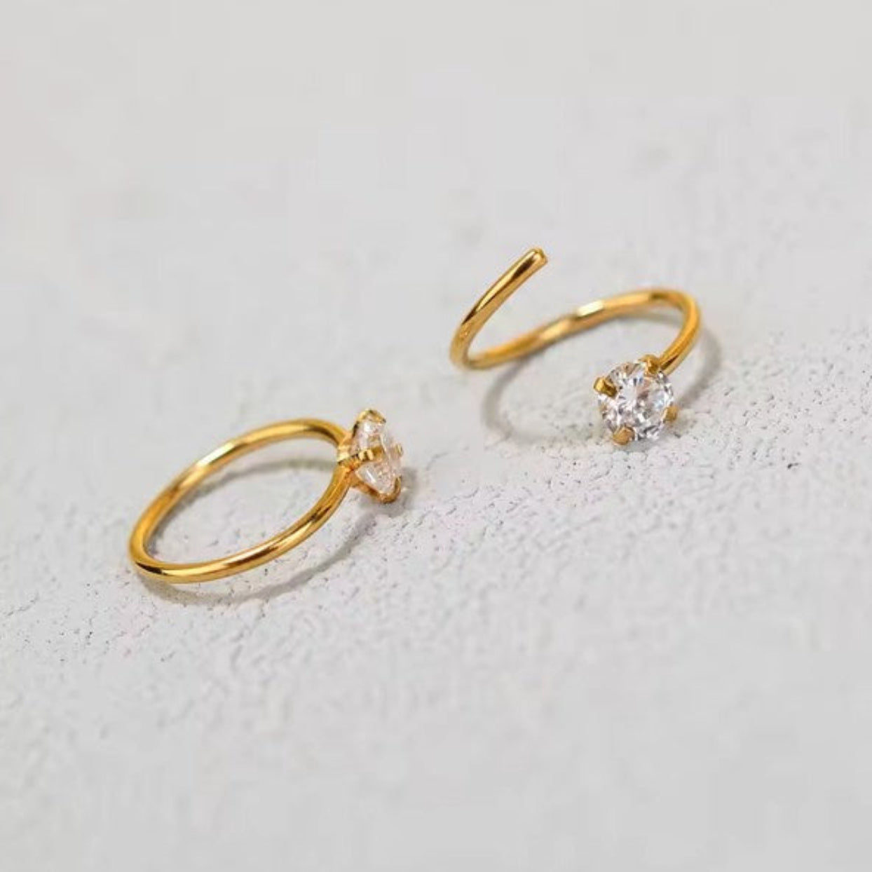 Two gold hoop earrings with clear gemstones on a light gray background