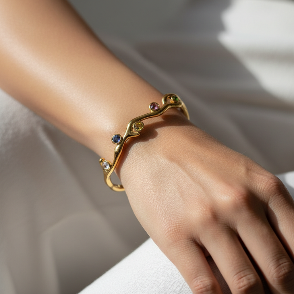 Gold bracelet with gemstones on a wrist against a neutral background