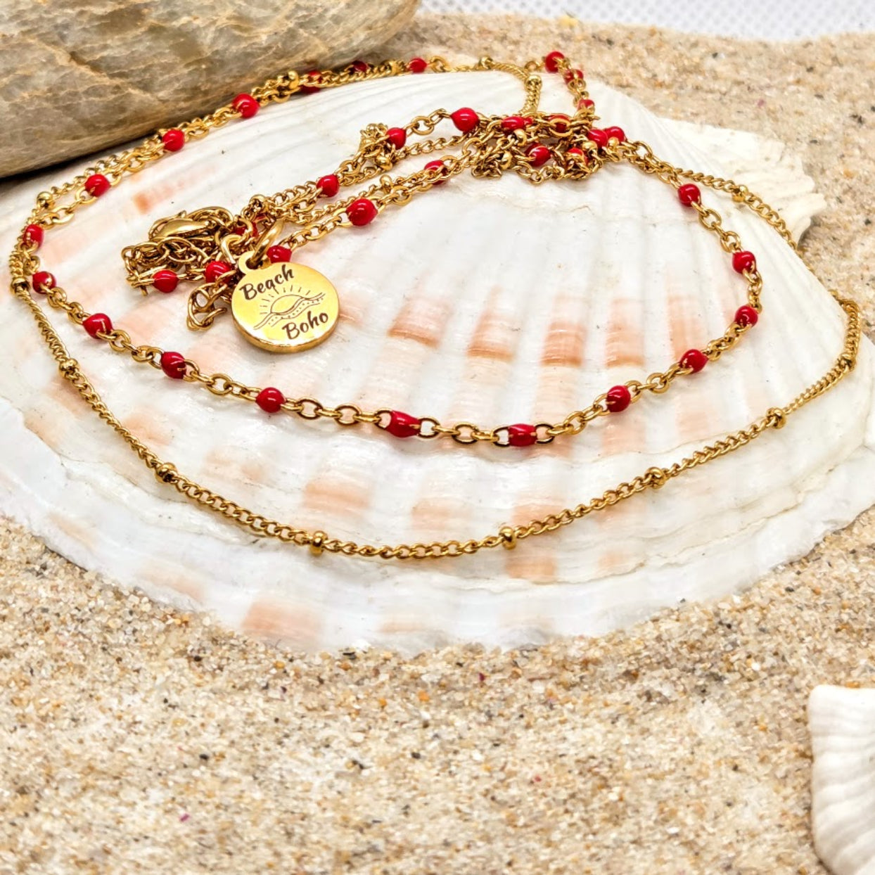 Gold necklace with red beads on a seashell with sand background