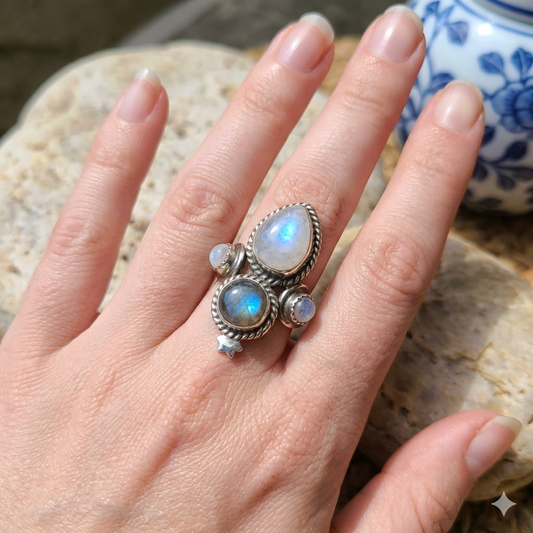 Hand wearing a silver ring with moonstone stones on a stone surface