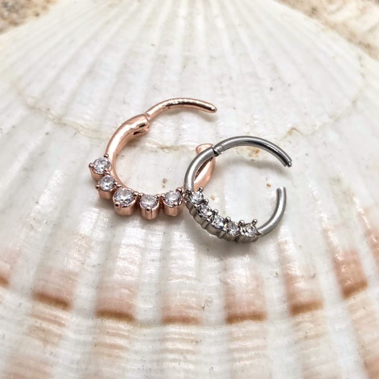 Two hoop earrings, one rose gold and one silver, on a seashell background.