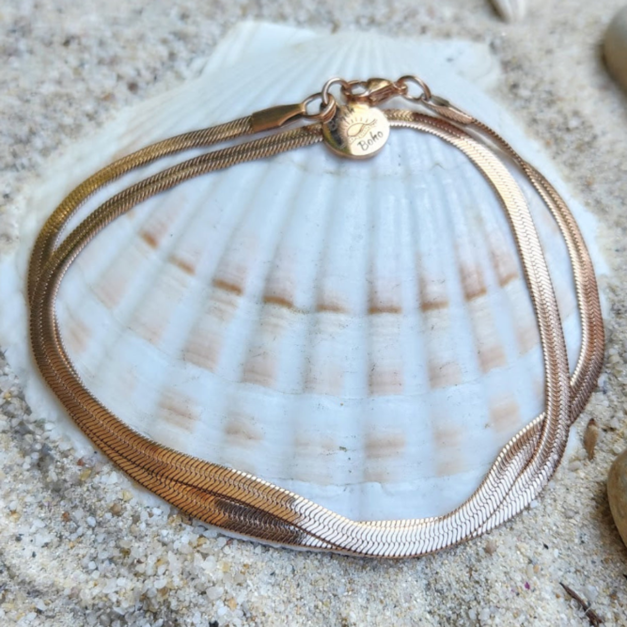 Gold necklace on a seashell with sand in the background
