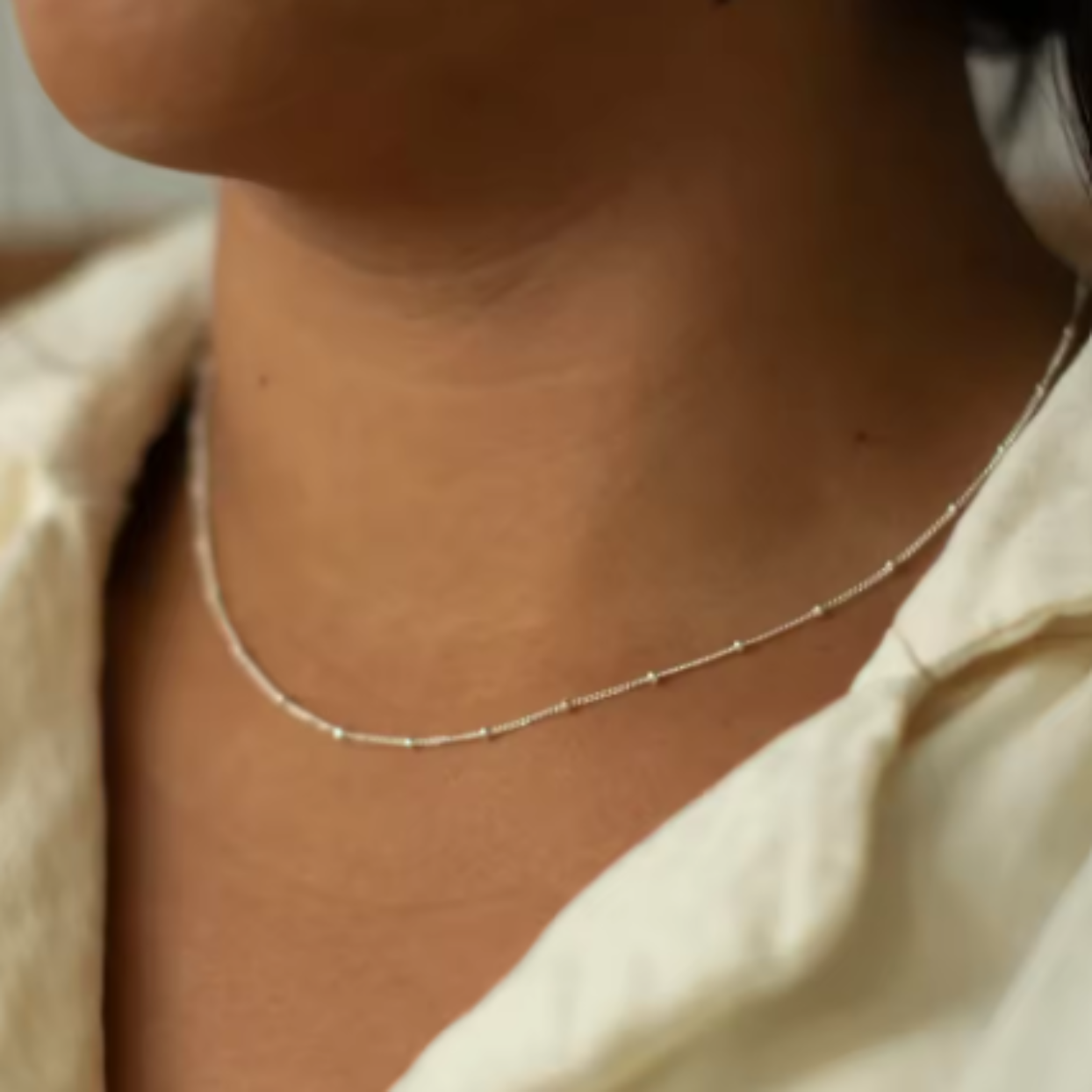 Close-up of a delicate gold necklace on a person wearing a light-colored shirt.