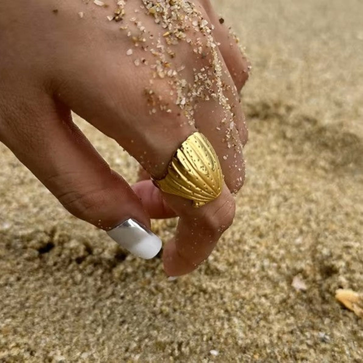 Hand holding a gold ring with sand on the background