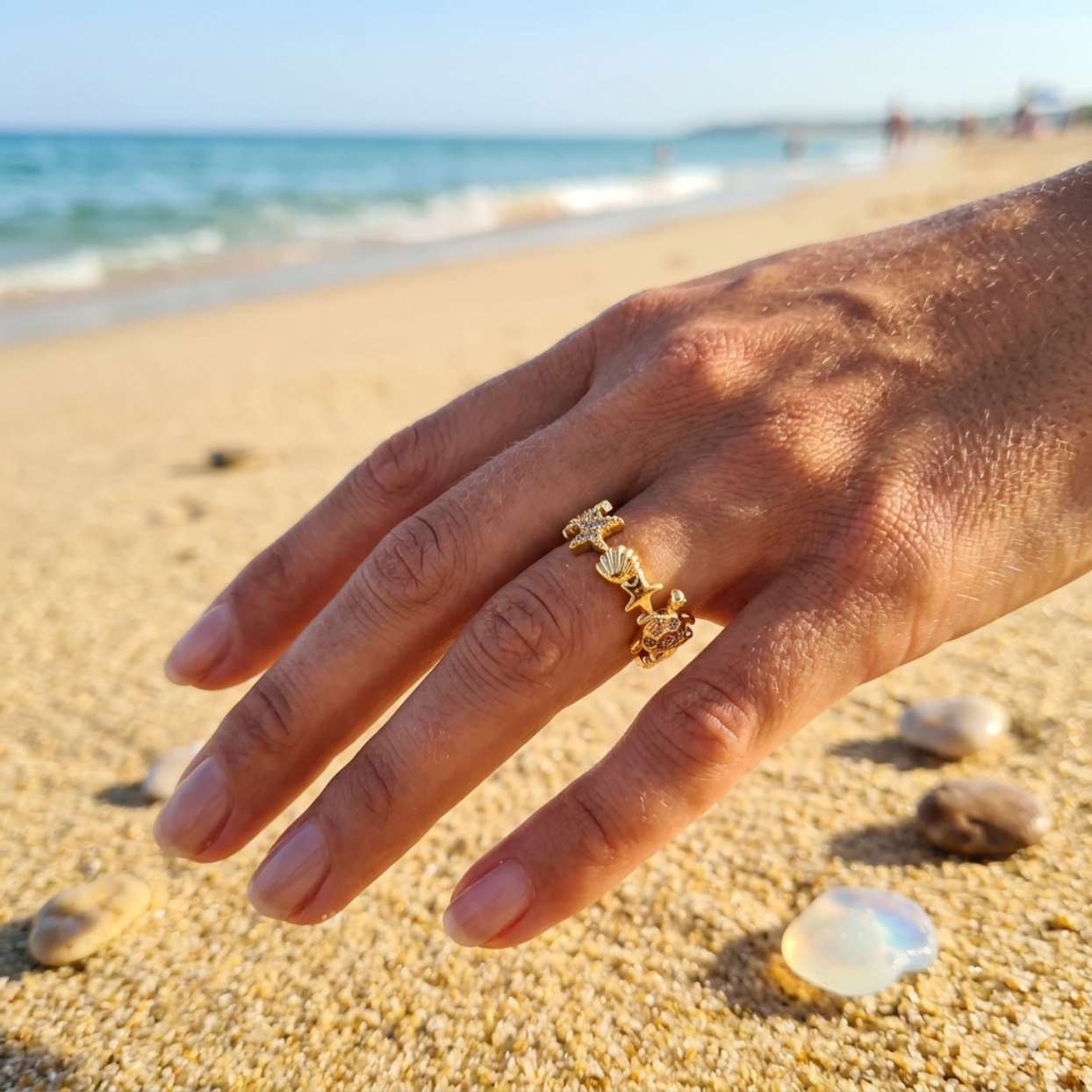 Hand wearing a gold ring on a sandy beach with ocean in the background