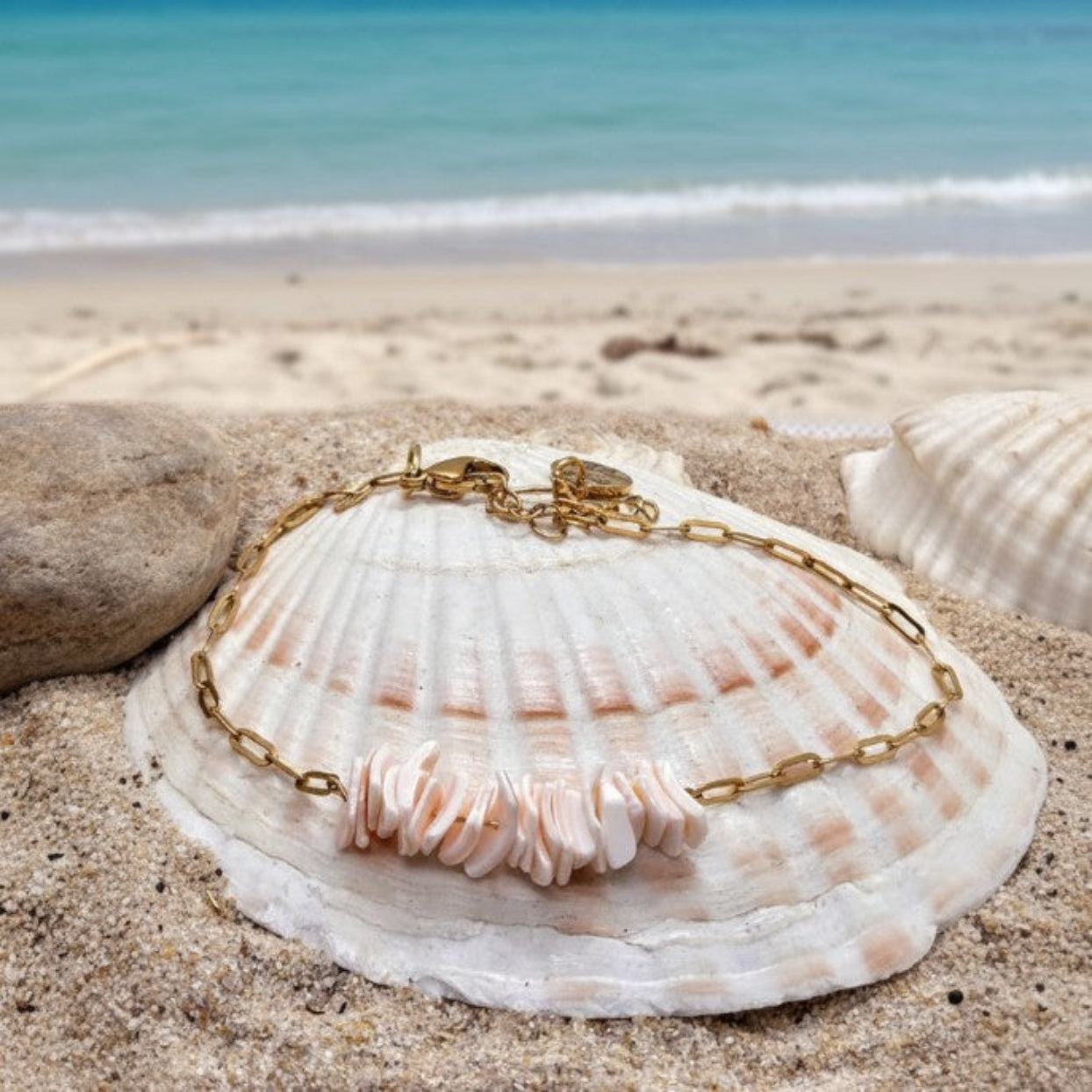 Gold bracelet with a shell charm on a seashell on a sandy beach.