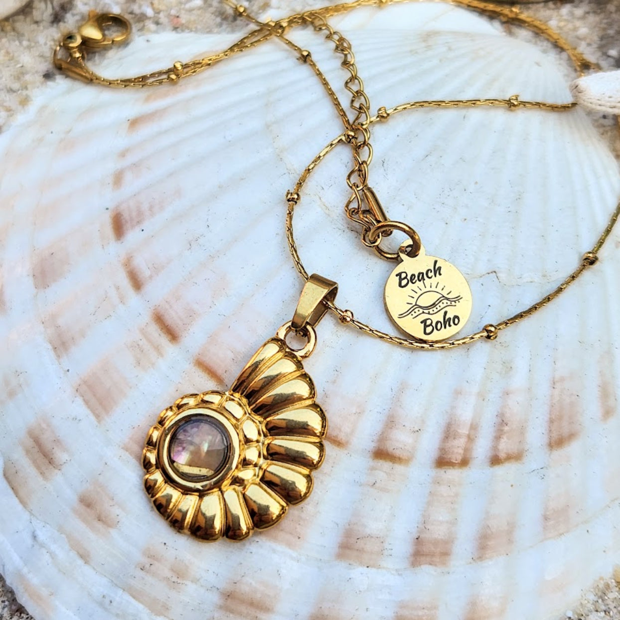 Gold necklace with a pendant and 'Beach Boho' tag on a seashell background